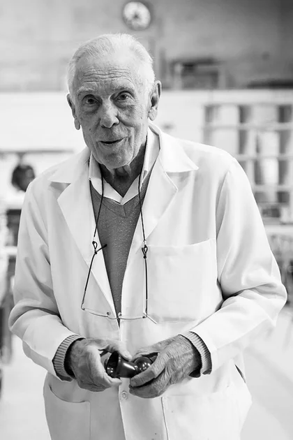 Retrato em preto e branco de Zezito, de jaleco branco, dentro da fábrica